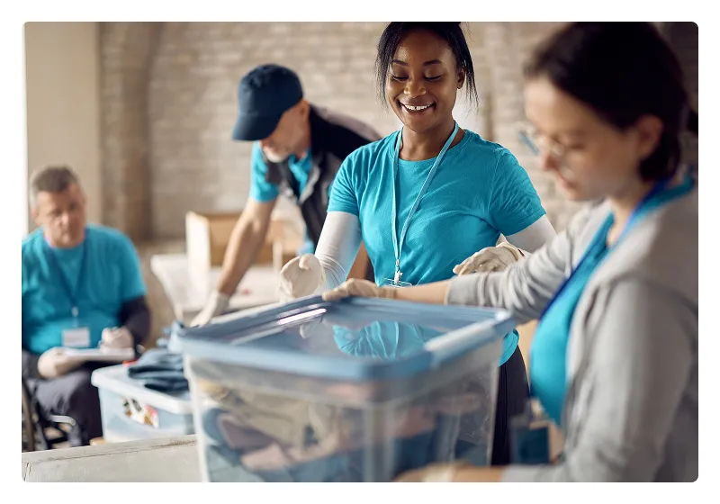 Group of volunteers sorting items into plastic bins in a community center.