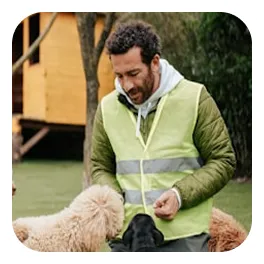 Man in a green reflective vest feeding and interacting with three dogs outdoors.