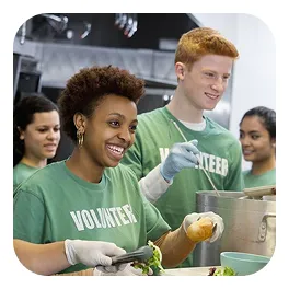Smiling volunteers in green shirts serving food in a community kitchen.