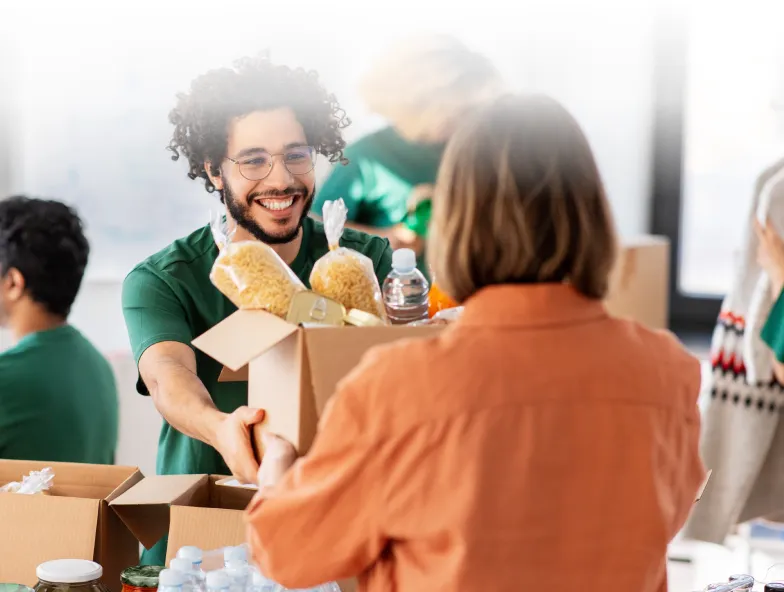 Smiling volunteer handing over a box of food supplies to a woman during a community food drive.