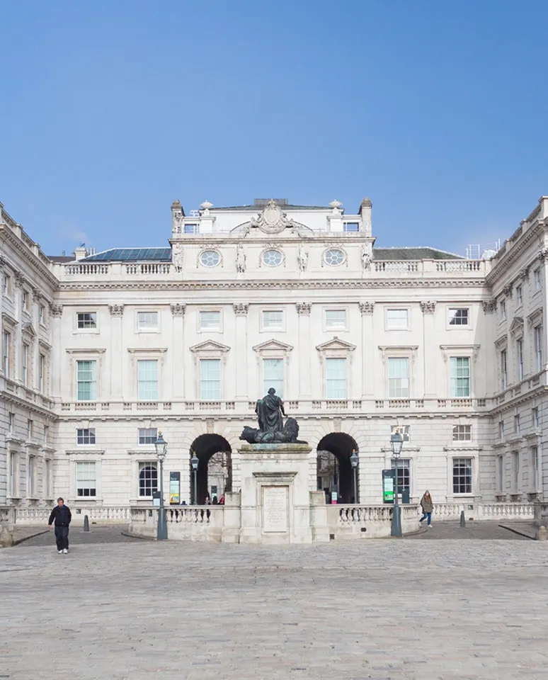 Historic white stone building with arched entrances and a statue in the center courtyard under a clear blue sky.