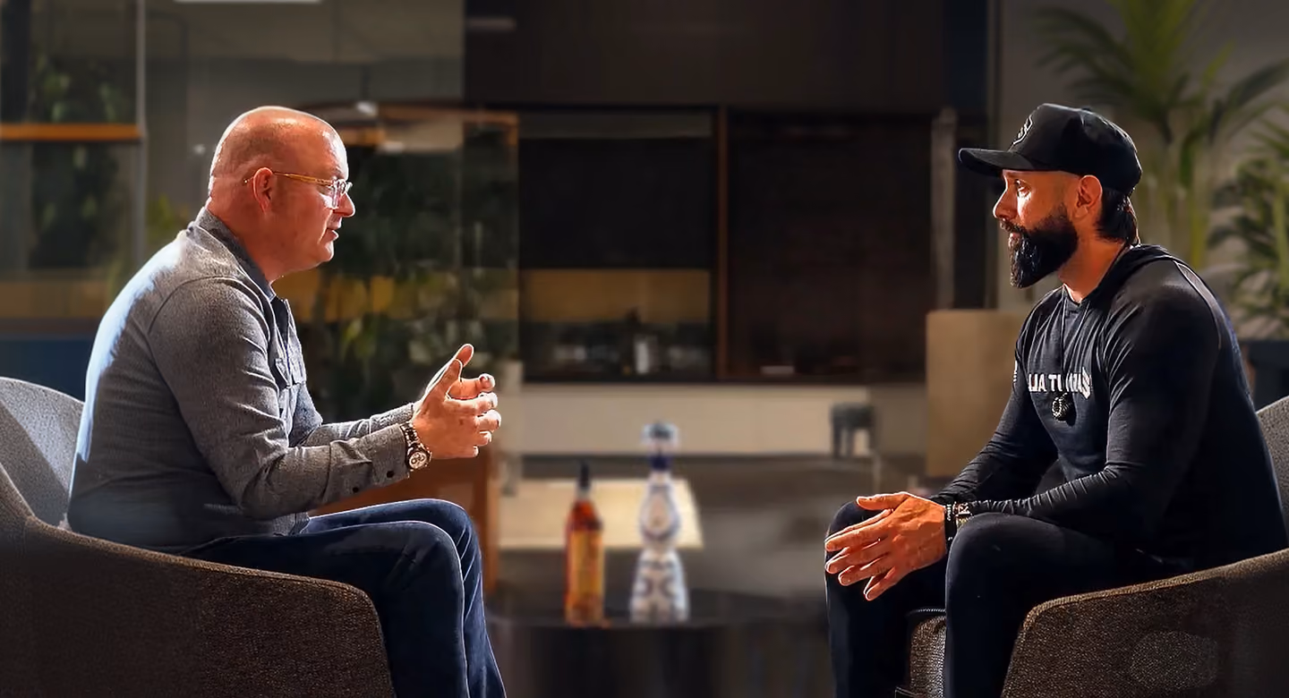 Two men sitting in chairs facing each other, engaged in conversation in a modern indoor setting.