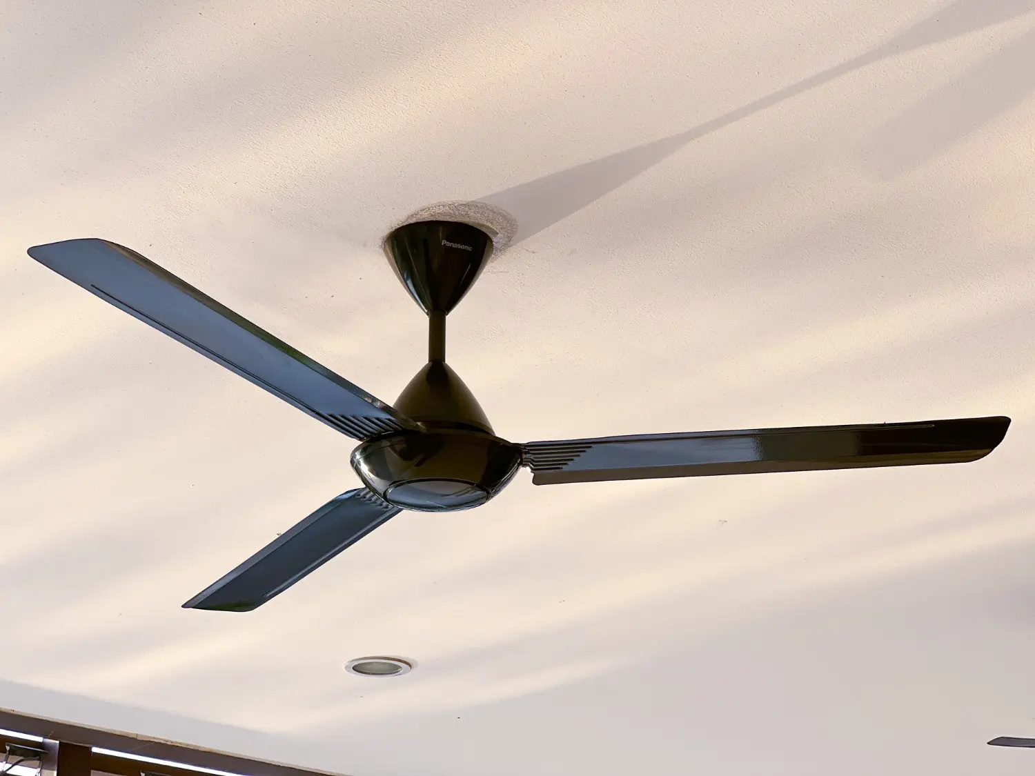 A sleek black three-blade Panasonic ceiling fan mounted on a white ceiling.