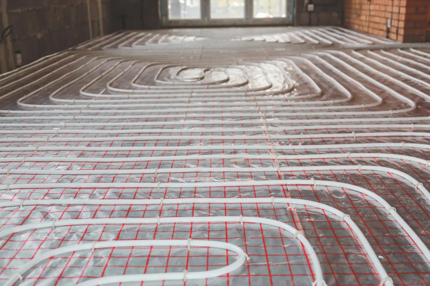 A room under renovation has PEX tubing laid on the subfloor, partially encased in concrete for radiant heating.