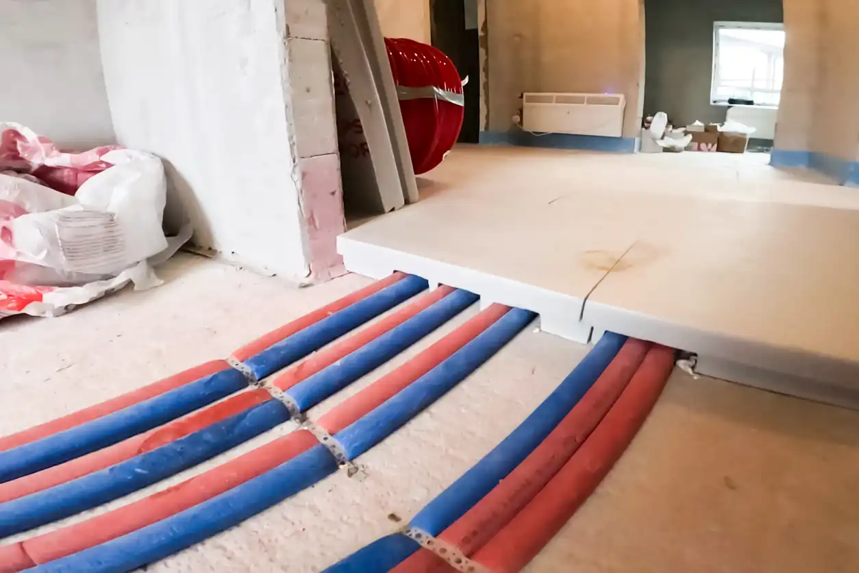 Insulated blue and red pipes running across a construction site floor and through a wall opening.