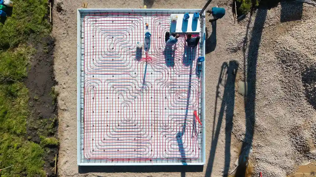Aerial view of a large concrete foundation slab with a complex grid of red radiant heating pipes installed.