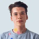 Portrait of a young man with short brown hair wearing a gray sweatshirt against a light background.