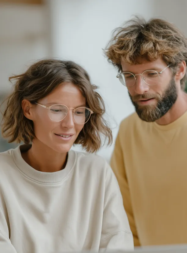 A man and woman wearing glasses looking at a laptop together indoors.