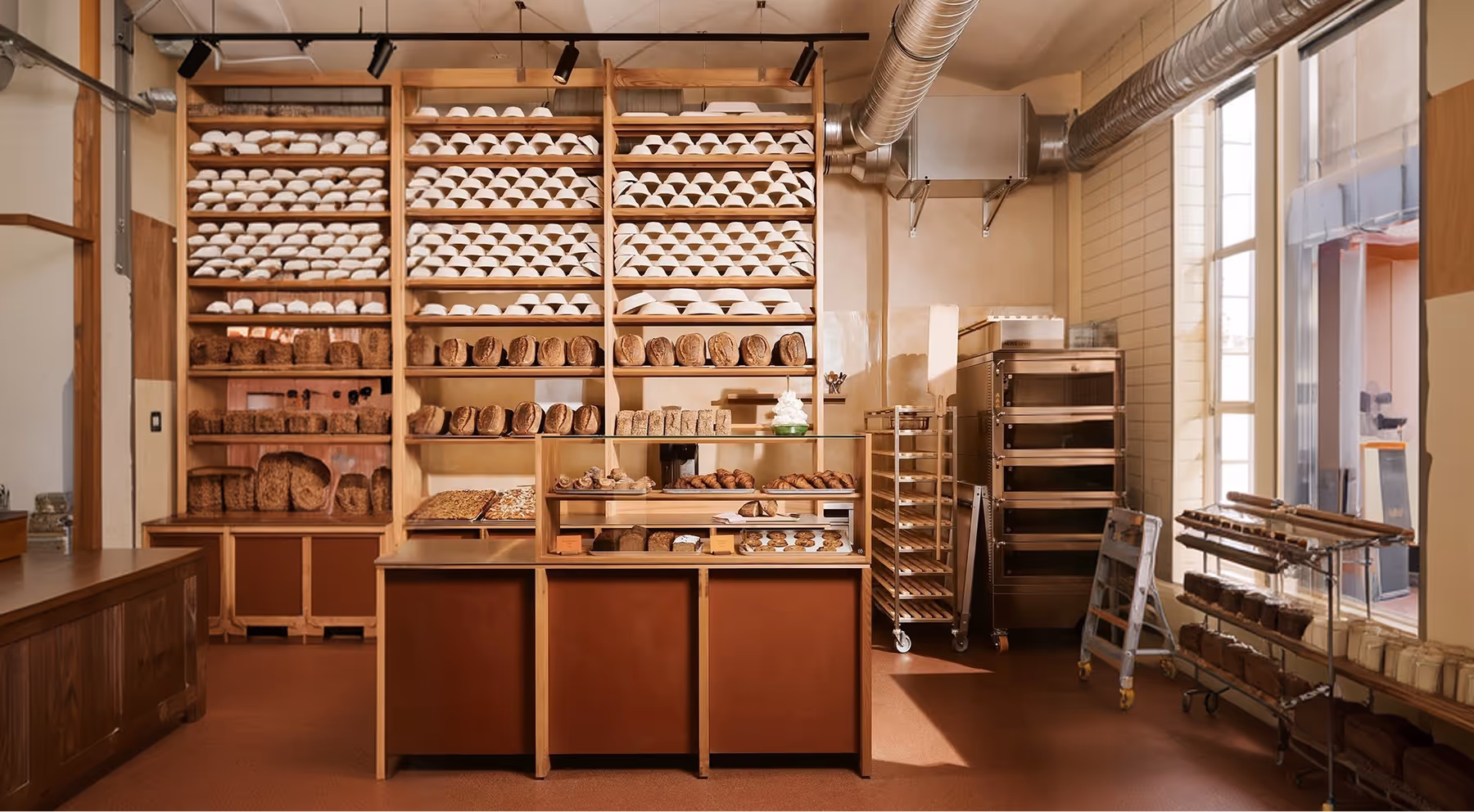 Intérieur d'une boulangerie avec étagères en bois remplies de pains variés, vitrine avec pâtisseries et four industriel à l'arrière.