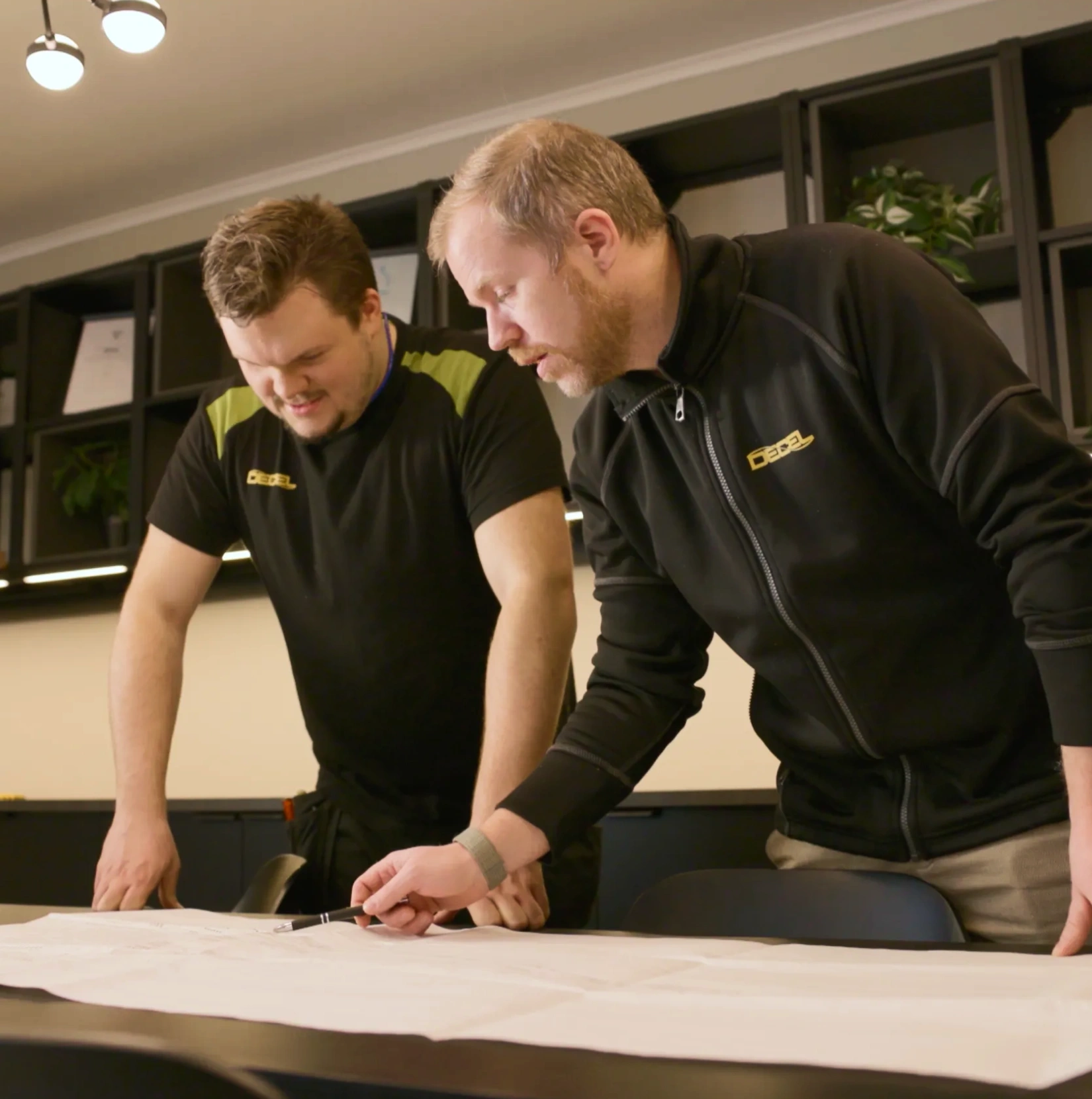 Två tekniker studerar en installationsritning för Decels spiralbroms vid en arbetsbänk.