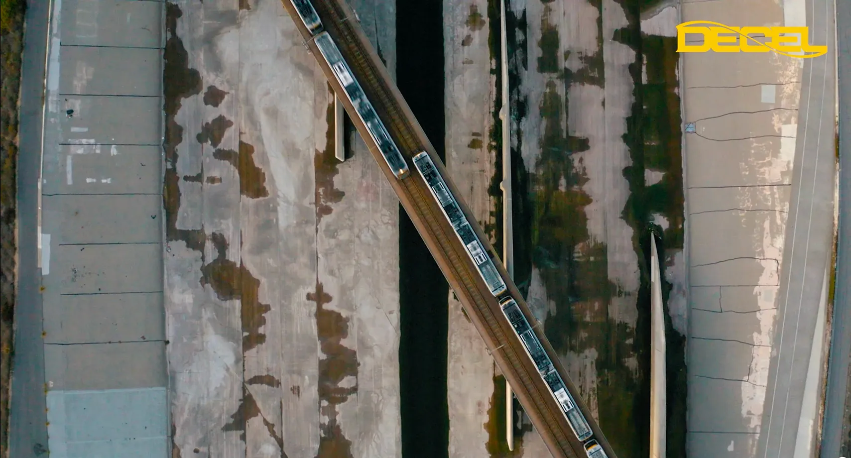 Flygbild av ett tåg som korsar en järnvägsbro över en betongkanal