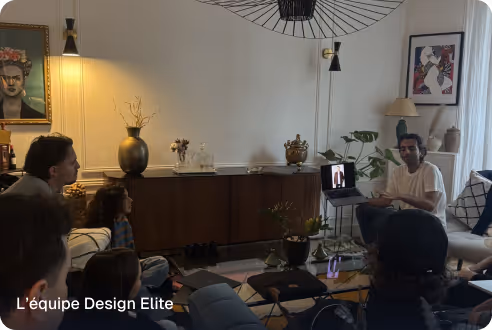 Several people seated in a living room engaged in a discussion, with one person presenting using a laptop.