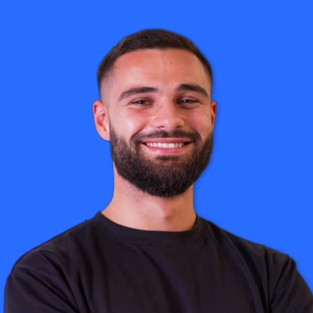 Smiling man with short dark hair and beard wearing a black shirt against a blue background.