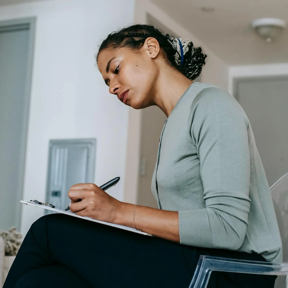 Femme assise écrivant sur un clipboard avec un stylo dans un intérieur clair.