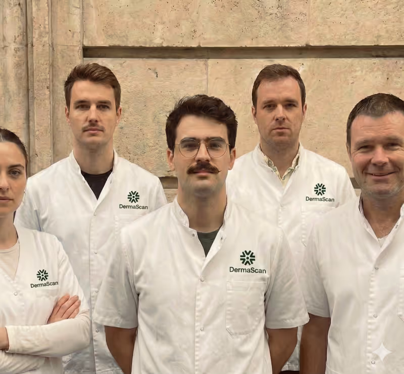 Groupe de professionnels en blouses blanches avec logo DermaScan, debout devant un mur en pierre.