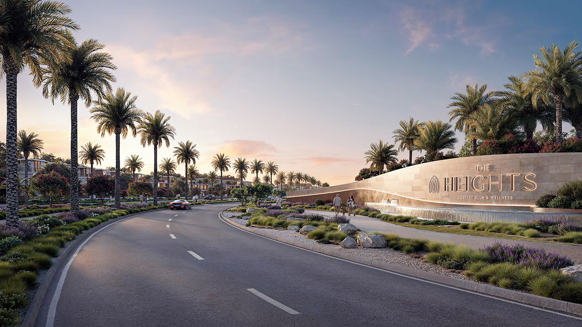 Entrance render of The Heights Country Club & Wellness by Emaar with landscaped boulevard, water feature, palm trees and illuminated project signage at sunset