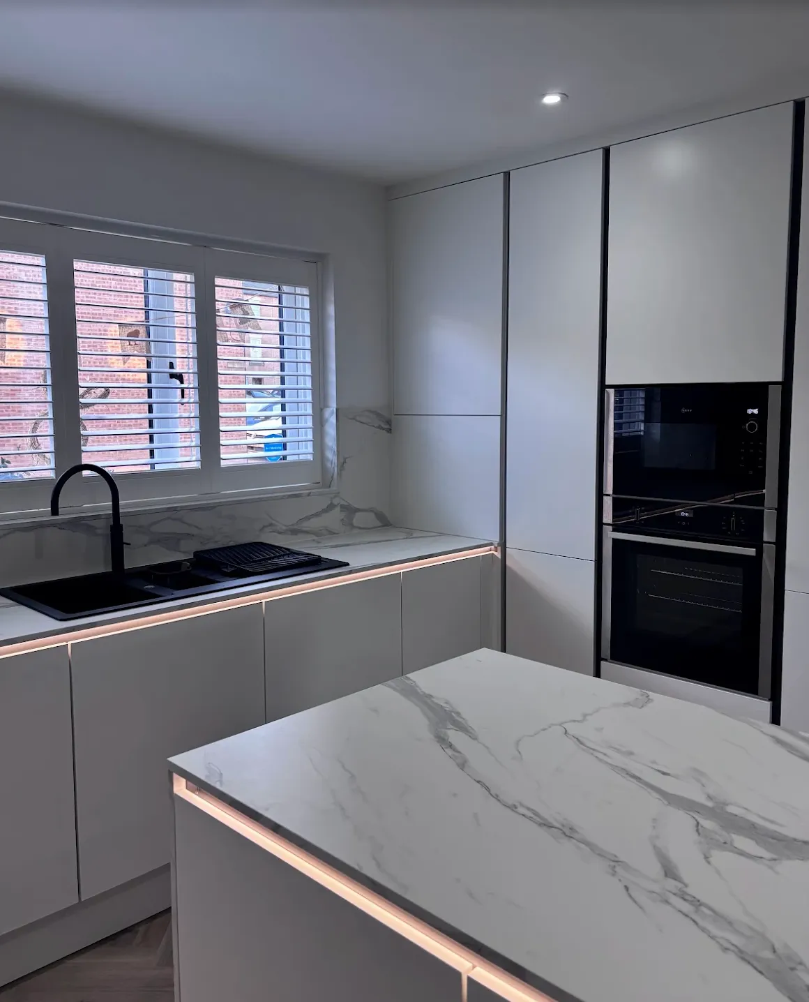 Modern kitchen with white marble countertops, black sink and faucet, built-in black oven and microwave, and white cabinets with under-cabinet lighting in Sheffield