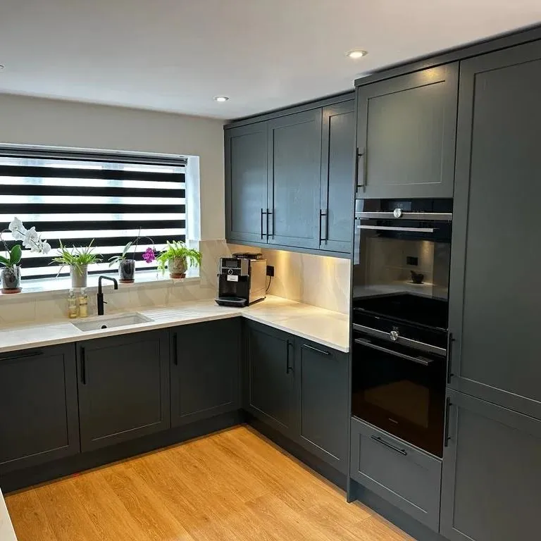 Modern kitchen with dark grey cabinets, light marble countertops, built-in black double oven, wooden floor, and window with black and white striped blinds. South Yorkshire