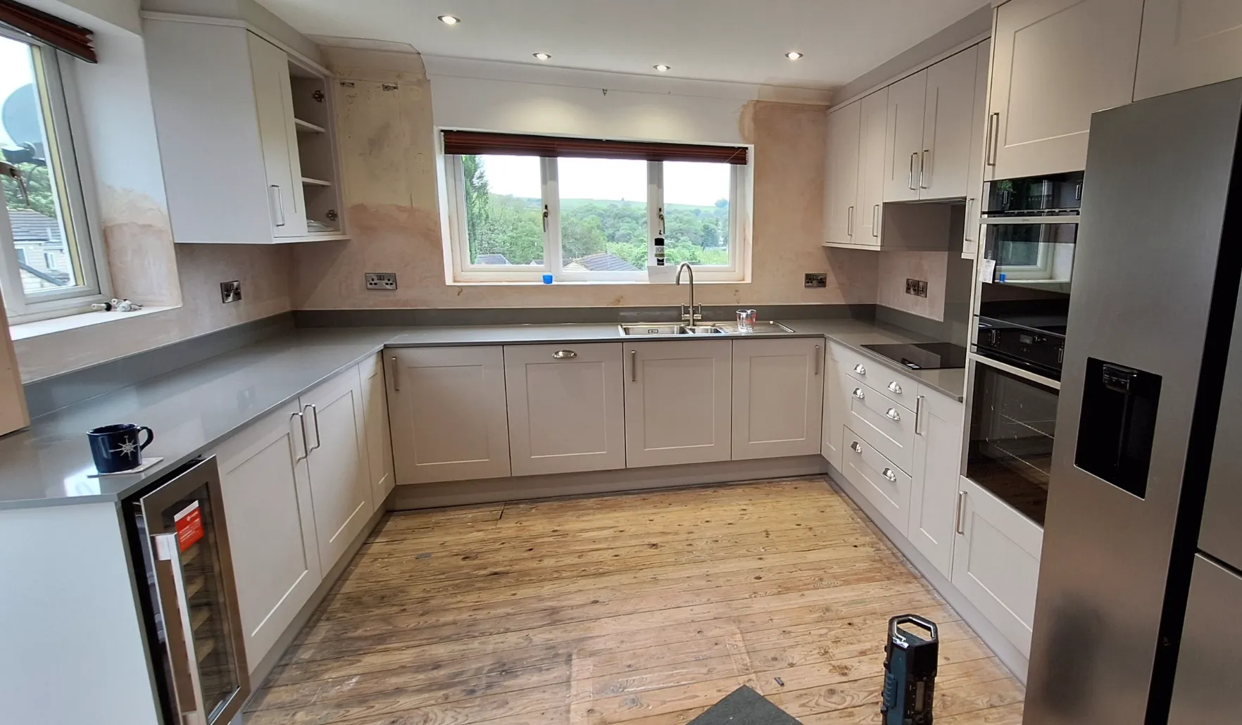 Modern kitchen with light gray cabinets, stainless steel appliances, double sink under a large window, and unfinished wooden floor in South Yorkshire