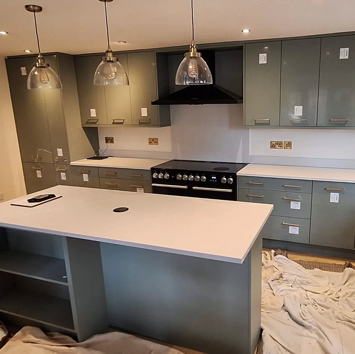 Modern kitchen with green cabinets, white countertops, a black range cooker, and three hanging pendant lights above a central island.