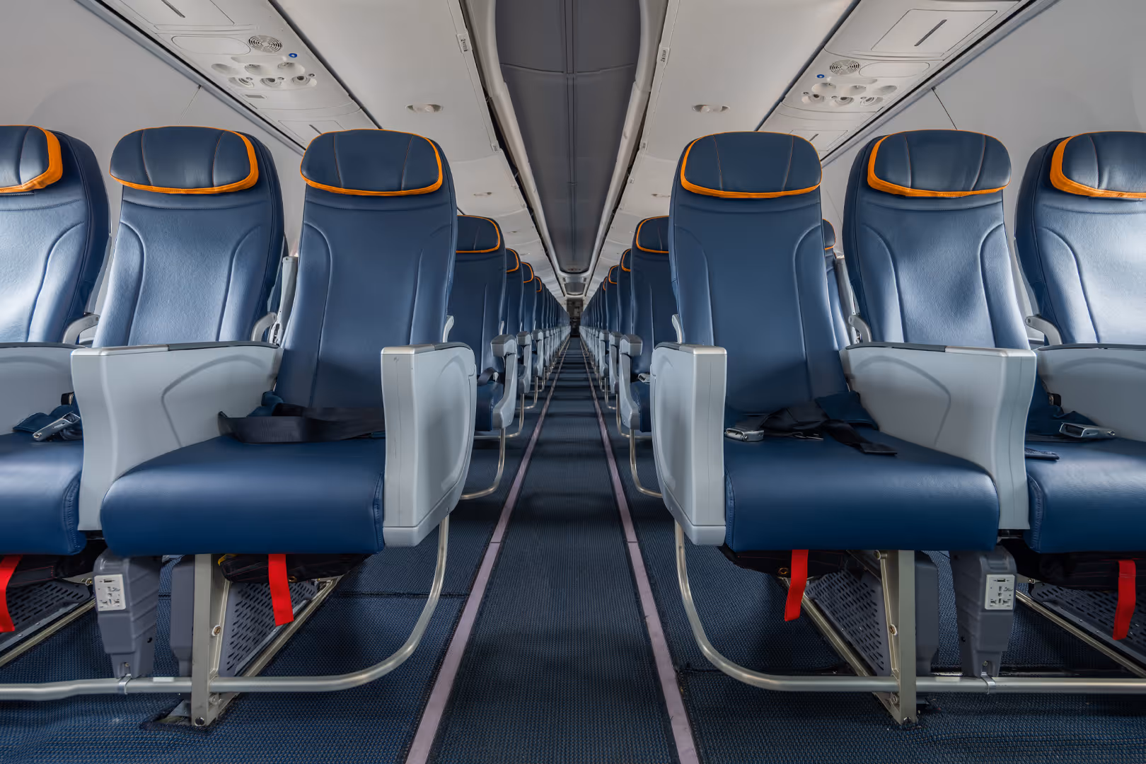Empty airplane cabin with rows of blue leather seats featuring orange trim and seat belts.