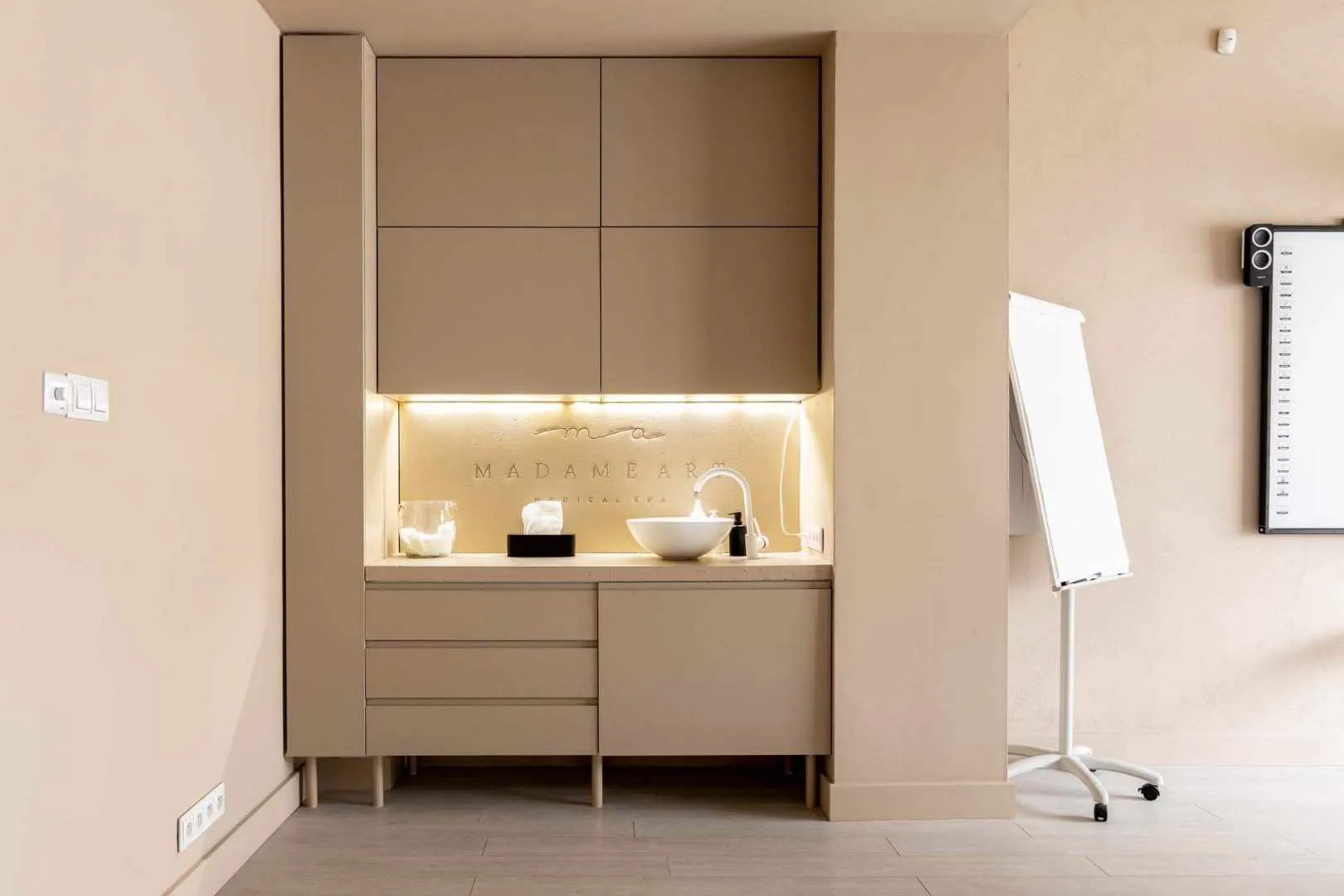 Minimalistyczna przestrzeń ze zlewem, szafkami oraz tablicą i flipchartem na kółkach.