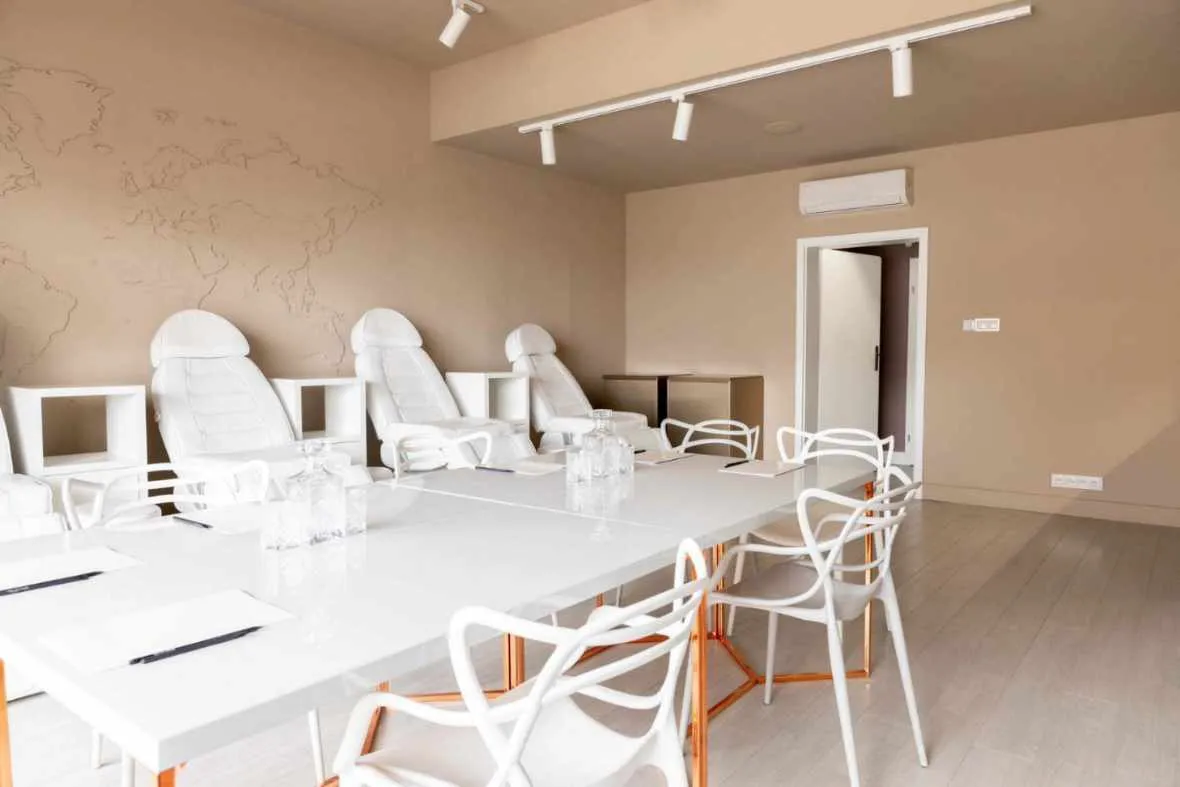 Nowoczesna sala konferencyjna z białymi krzesłami i fotelami na jasnobeżowej ścianie z mapą świata.