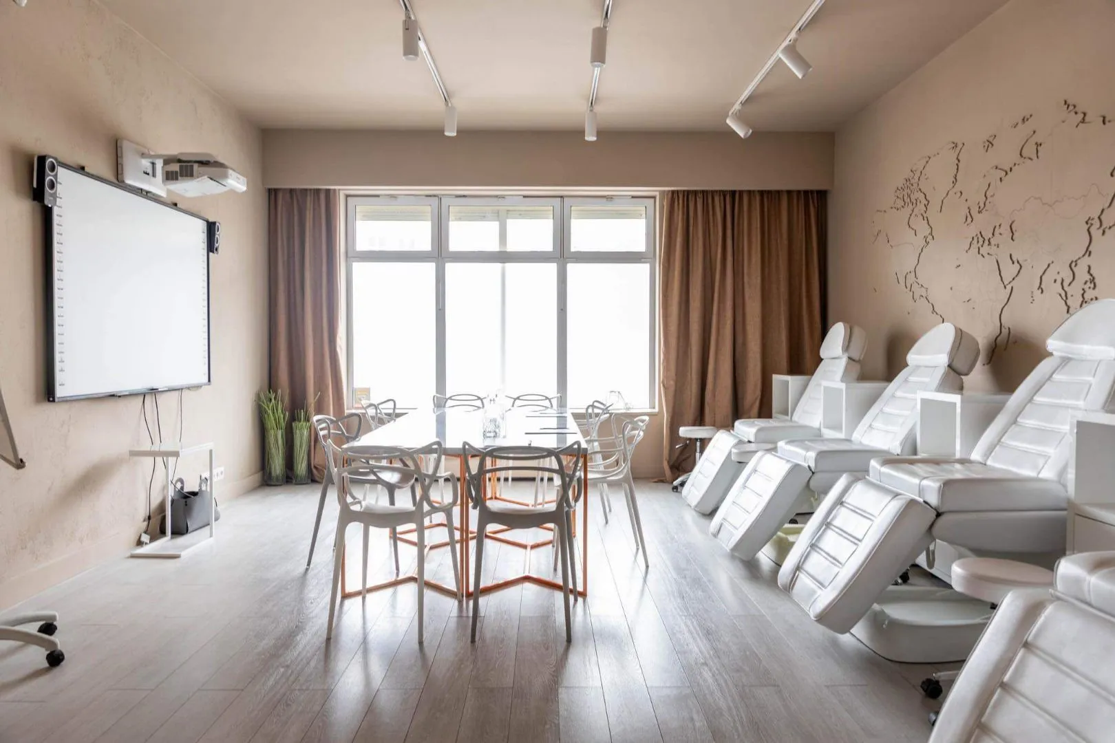 Nowoczesna sala konferencyjna z białymi krzesłami, stołem, ekranem projekcyjnym i fotelami medycznymi przy ścianie z mapą świata.
