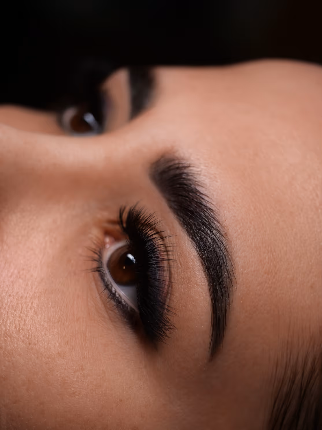 Zbliżenie na twarz z brązowymi oczami, gęstymi, ciemnymi rzęsami i starannie zaznaczonymi brwiami.