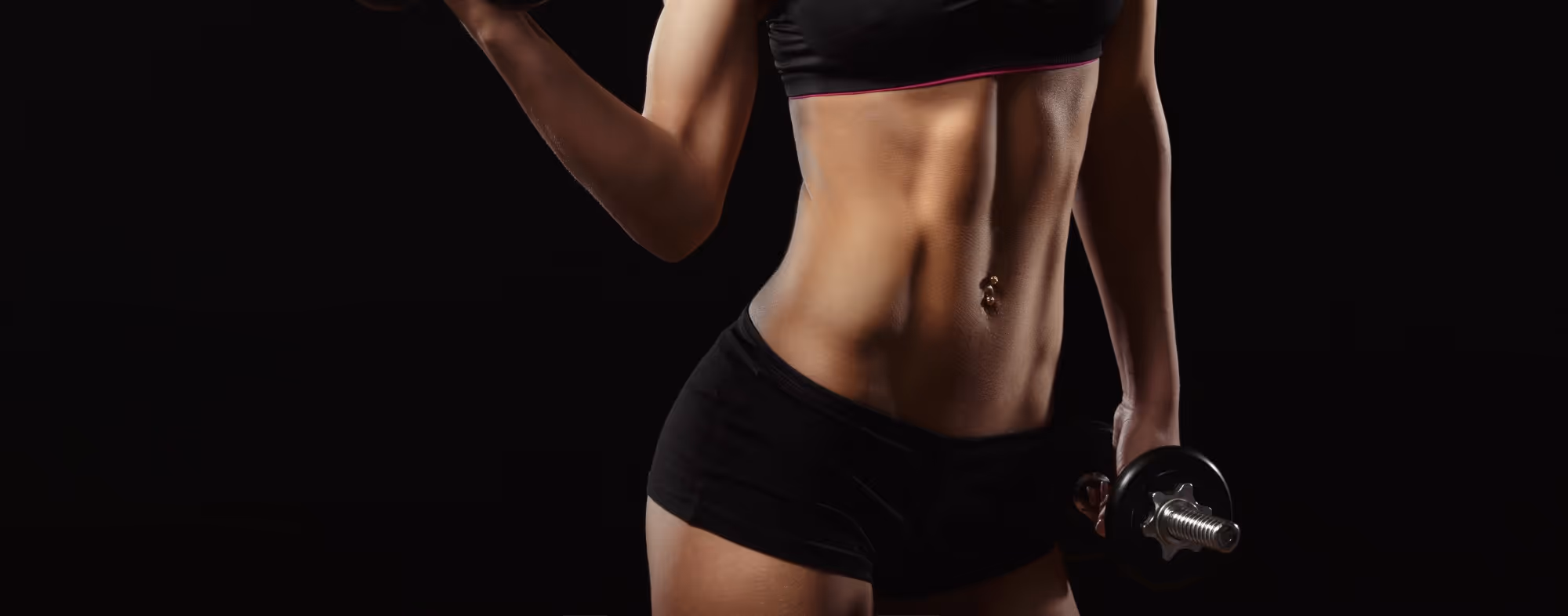 Szczupła kobieta w czarnym stroju sportowym trzyma hantlę na czarnym tle.