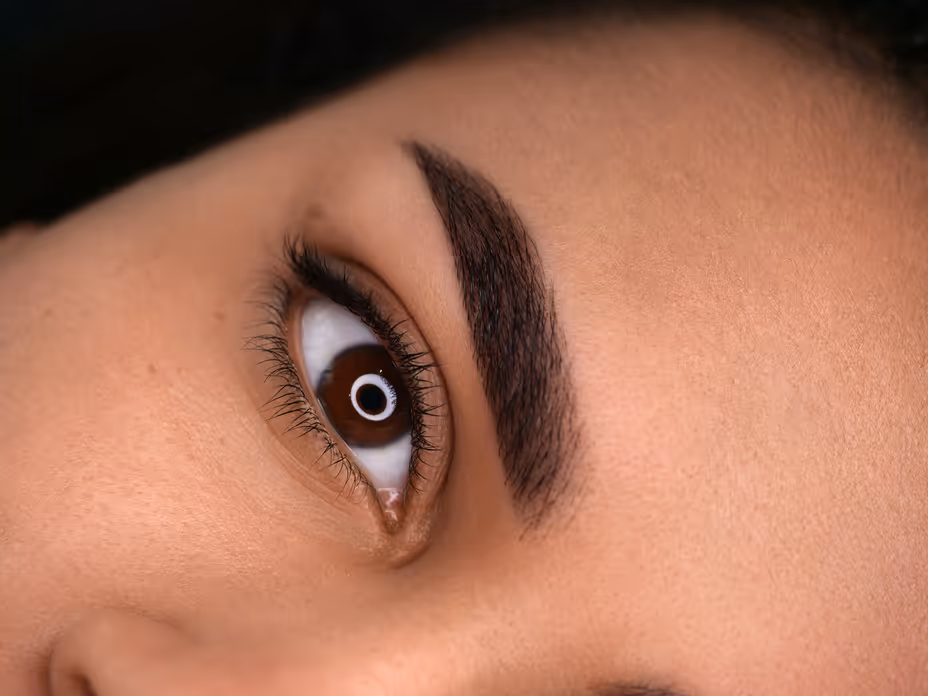 Zbliżenie na brązowe oko z gęstymi, ciemnymi brwiami i długimi rzęsami na jasnej skórze.