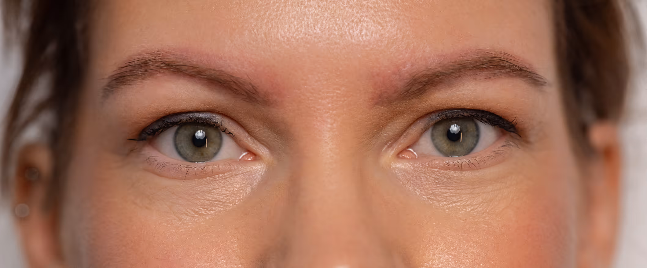 Zbliżenie na zielone oczy kobiety z delikatnym makijażem i naturalnymi brwiami.