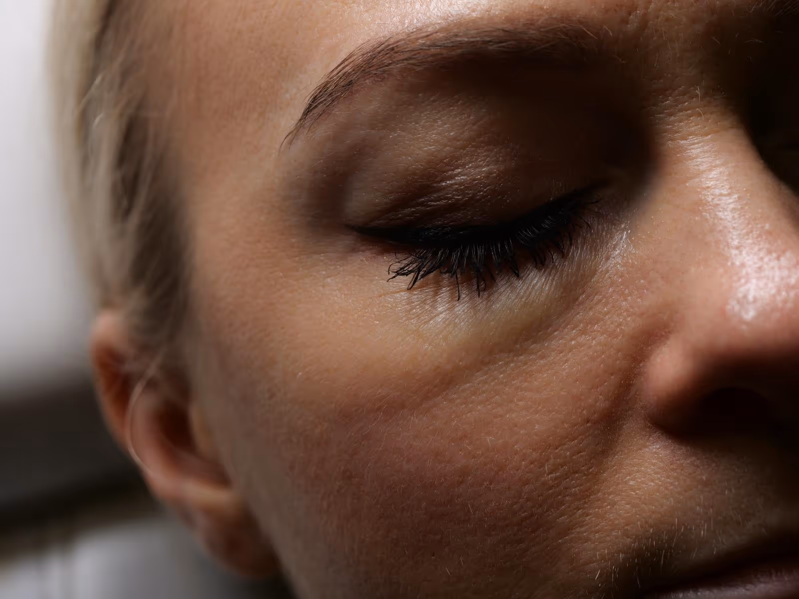 Zbliżenie na zamknięte oko kobiety z długimi rzęsami i delikatnym makijażem.