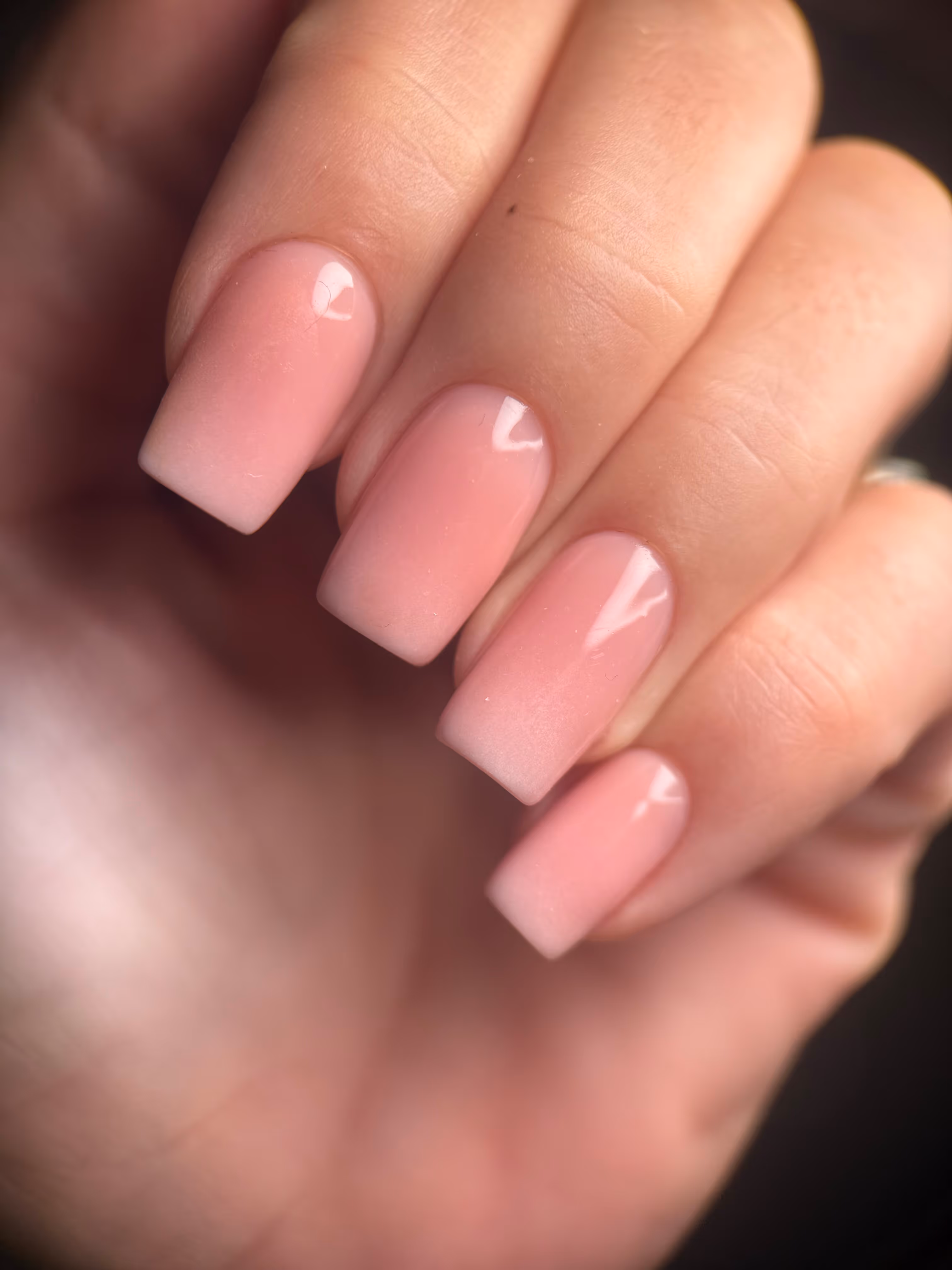 Dłonie z delikatnym, jasnoróżowym manicure w stylu ombre z kwadratowymi paznokciami.