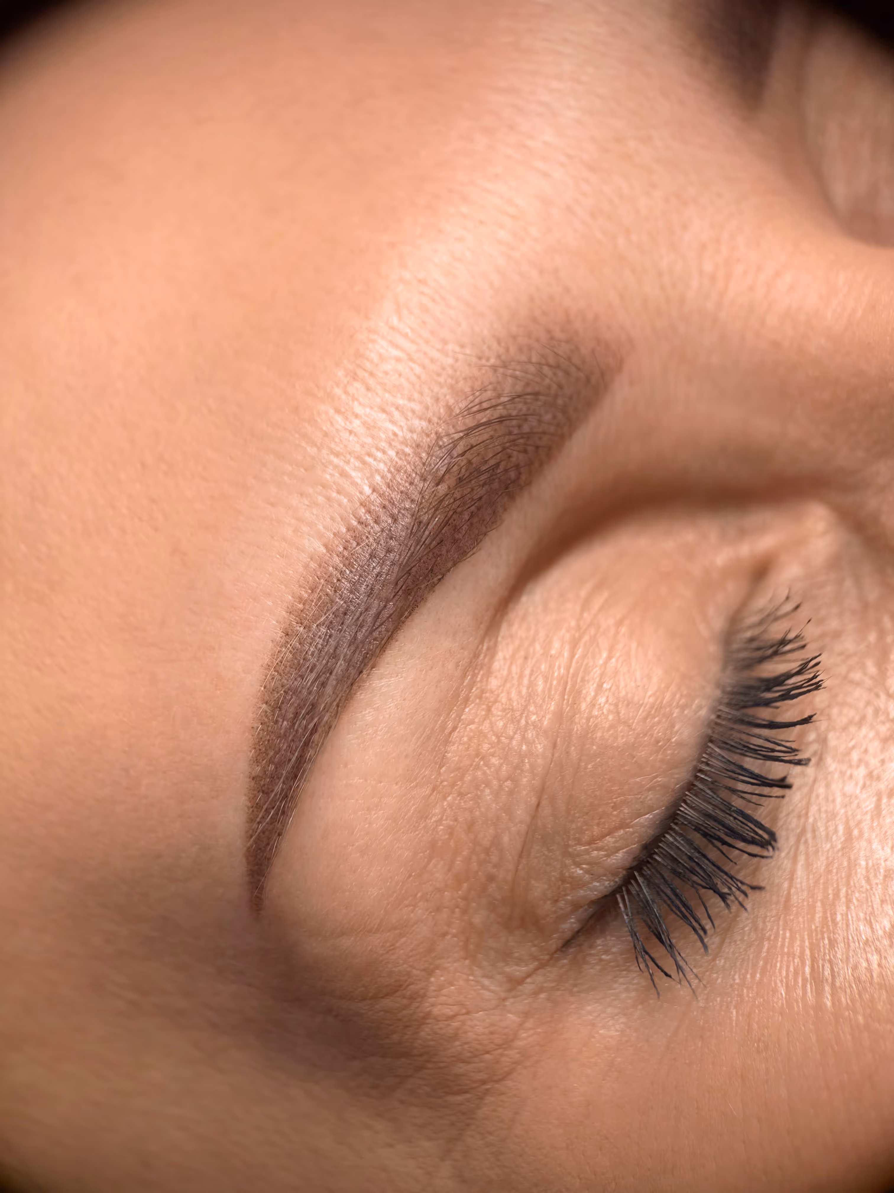 Zbliżenie na oko z zamkniętą powieką i podkreślonym brwiami oraz długimi rzęsami.