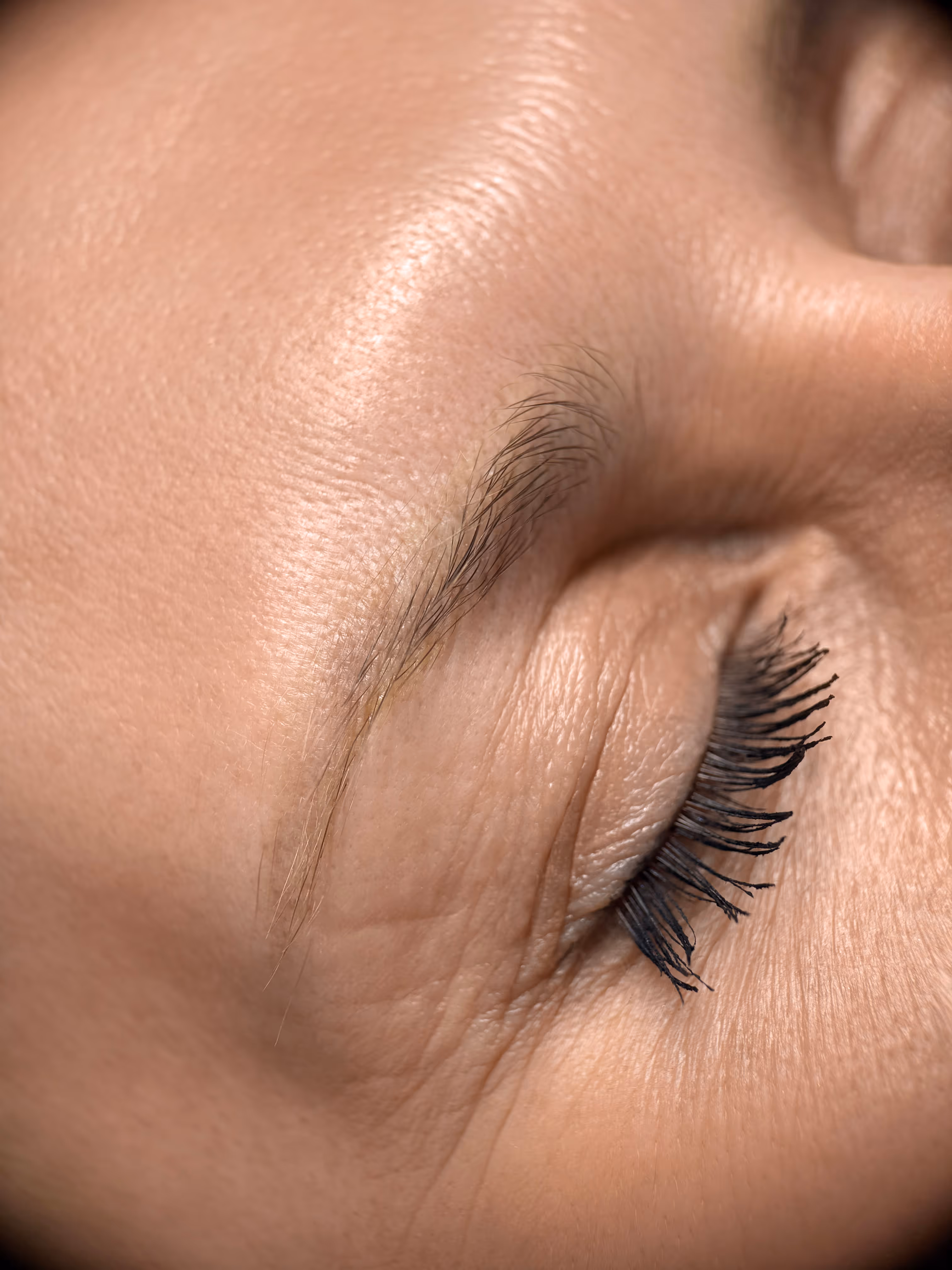 Zbliżenie na zamknięte oko kobiety z subtelnie podkreśloną czarnym tuszem rzęsą i naturalną brwią.