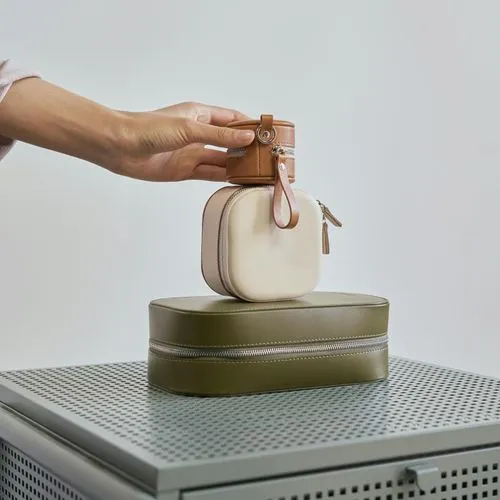 Hand holding a small brown and beige leather case stacked on top of a larger olive green leather case on a metal surface.