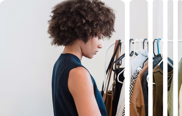 Woman with curly hair looking at clothes on a rack indoors.