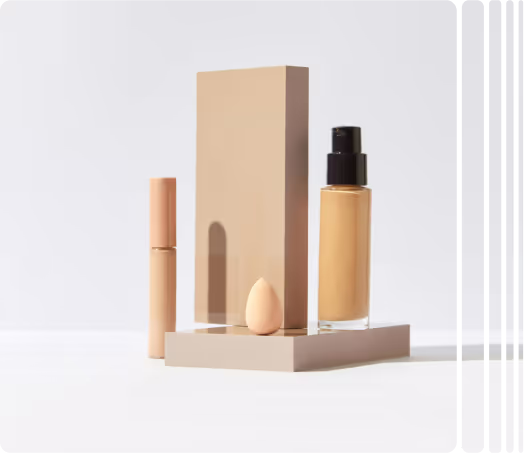Foundation makeup set with a bottle of liquid foundation, a small beige makeup sponge, and a concealer tube on beige stands.
