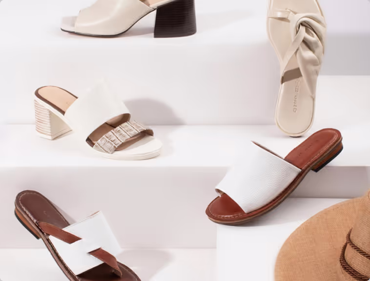 Variety of white and beige women's summer sandals displayed on white steps.