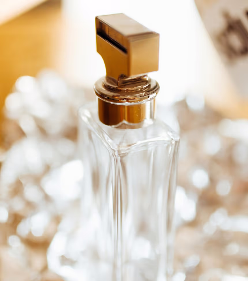 Close-up of a clear glass perfume bottle with a gold-colored rectangular cap.