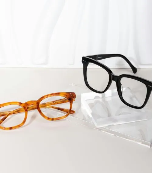 Two pairs of eyeglasses, one with tortoiseshell frames and one with black frames, displayed on a white surface.