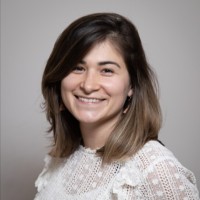 Portrait d'une femme souriante aux cheveux châtains portant un haut blanc en dentelle.