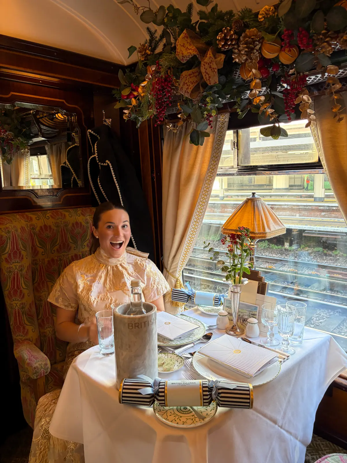 Barrett in elegant attire seated at a decorated dining table inside a vintage train carriage.