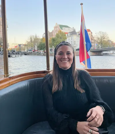 Barrett in a black sweater sitting on a boat with a Dutch flag and canal houses in the background.