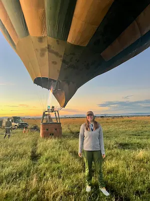 Barrett standing on grassy field near an inflated hot air balloon at sunrise or sunset.