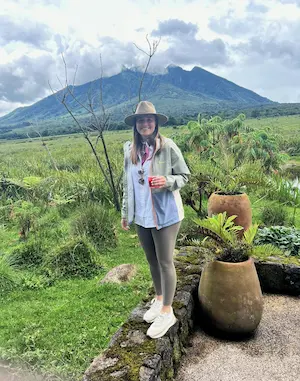 Barrett wearing a hat standing on a stone edge with green grass and mountains in the background under a cloudy sky.