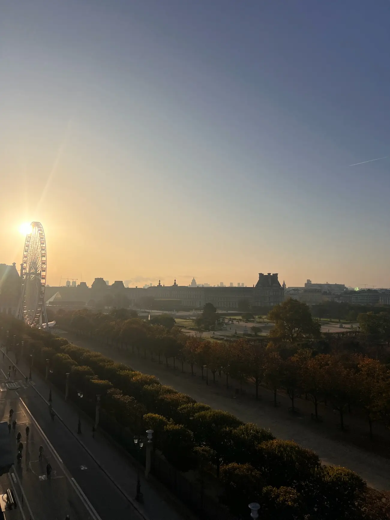 Sunset over Paris with the Ferris wheel near Tuileries Garden and the Louvre Museum silhouette in the background.