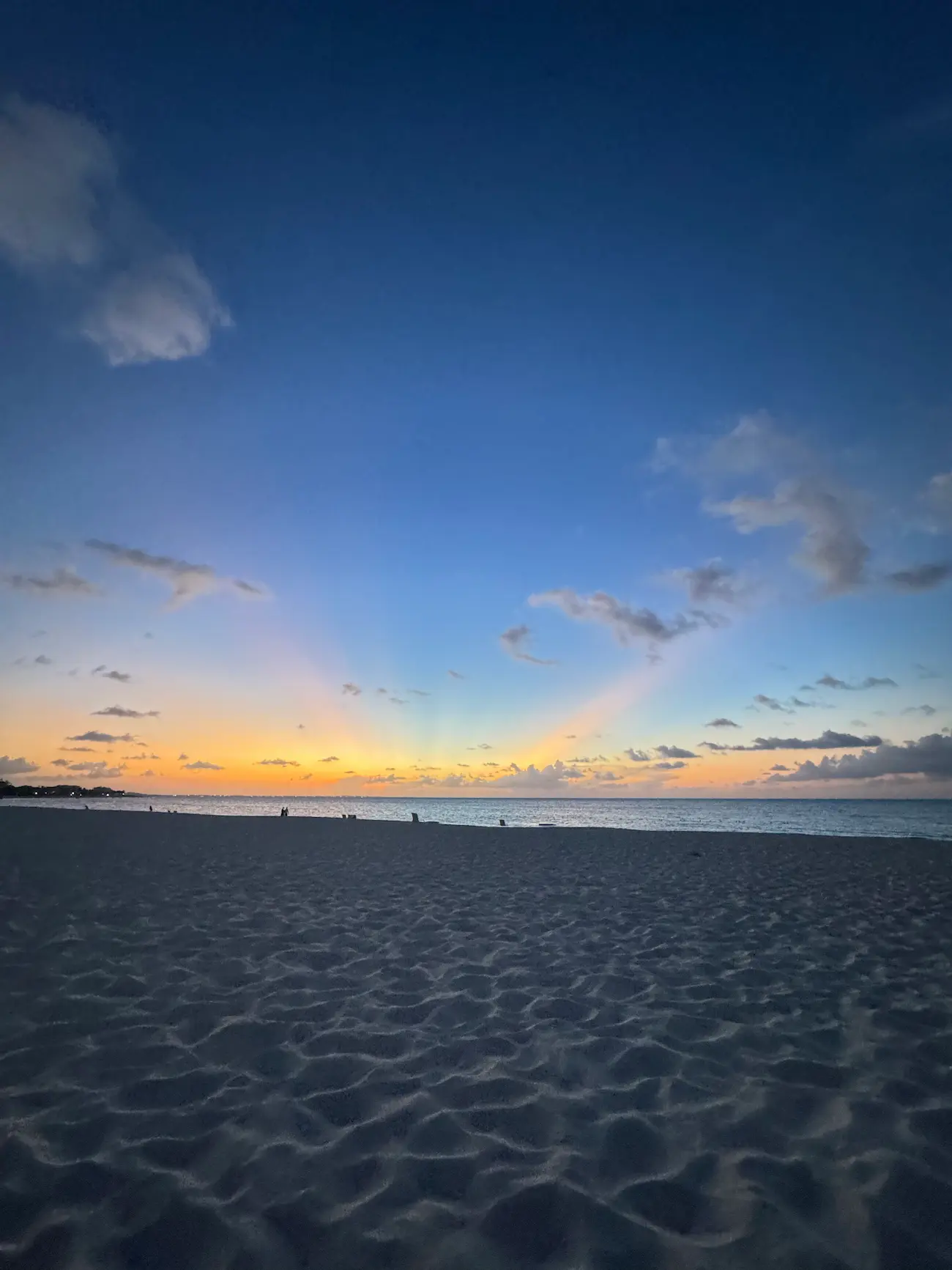 Sunset with orange and blue sky over a calm ocean and sandy beach with scattered clouds.