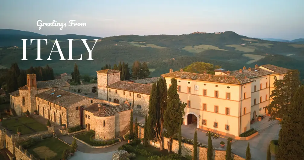 Aerial view of a rustic Italian villa and surrounding green hills at sunset with the text 'Greetings From ITALY'.